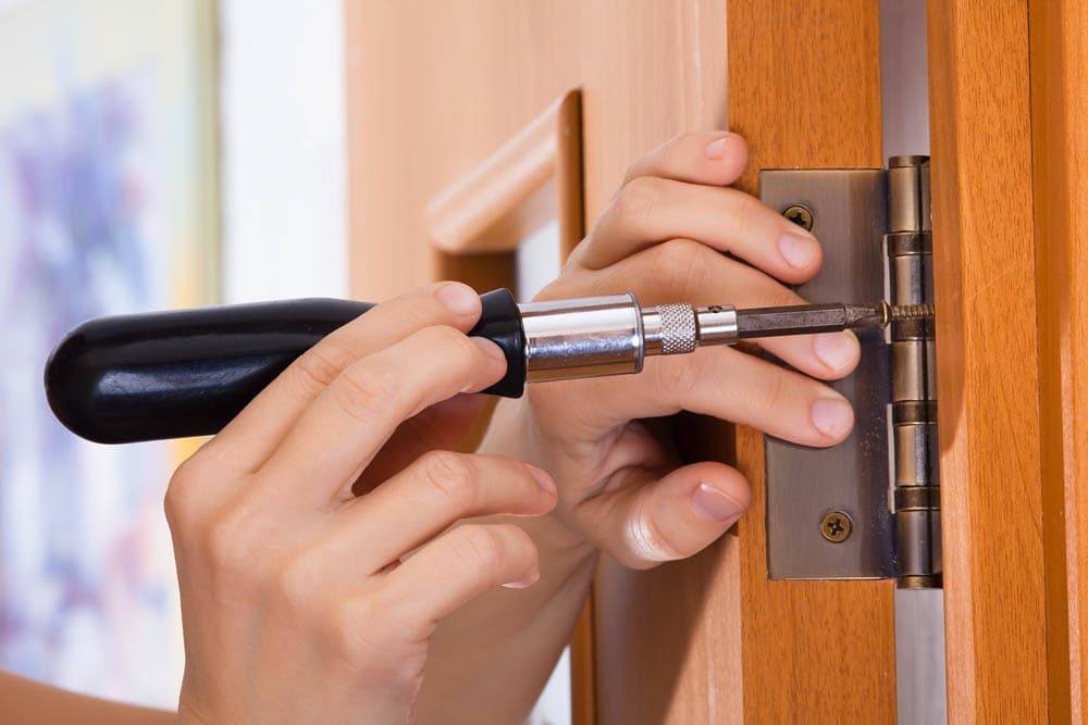 hands with screwdriver screwing hinge on a door, closeup